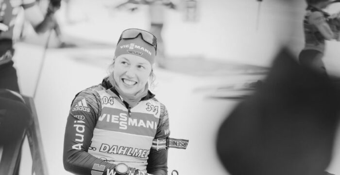 Die-Biathlonwelt-trauert-um-Laura-Dahlmeier Laura Dahlmeier im Rennanzug lächelt nach dem Wettkampf, Schwarz-Weiß-Aufnahme mit ruhigem Ausdruck.