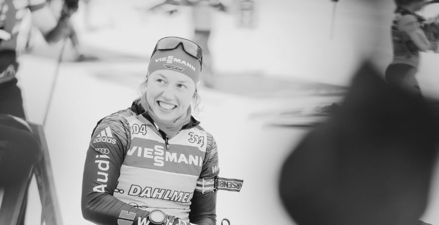 Laura Dahlmeier im Rennanzug lächelt nach dem Wettkampf, Schwarz-Weiß-Aufnahme mit ruhigem Ausdruck.