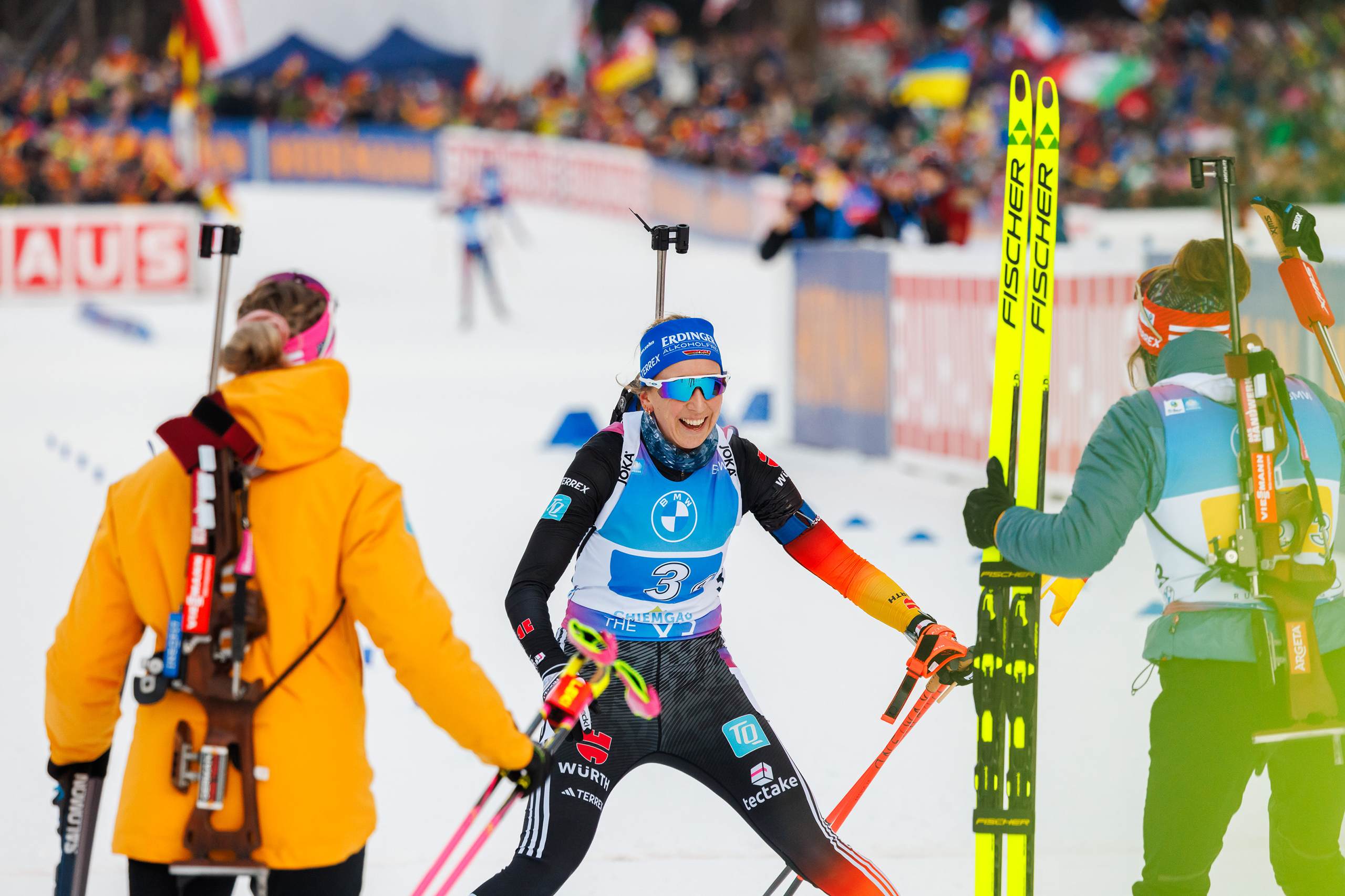 Biathletinnen der Frauenstaffel jubeln beim Wechsel im Stadion.