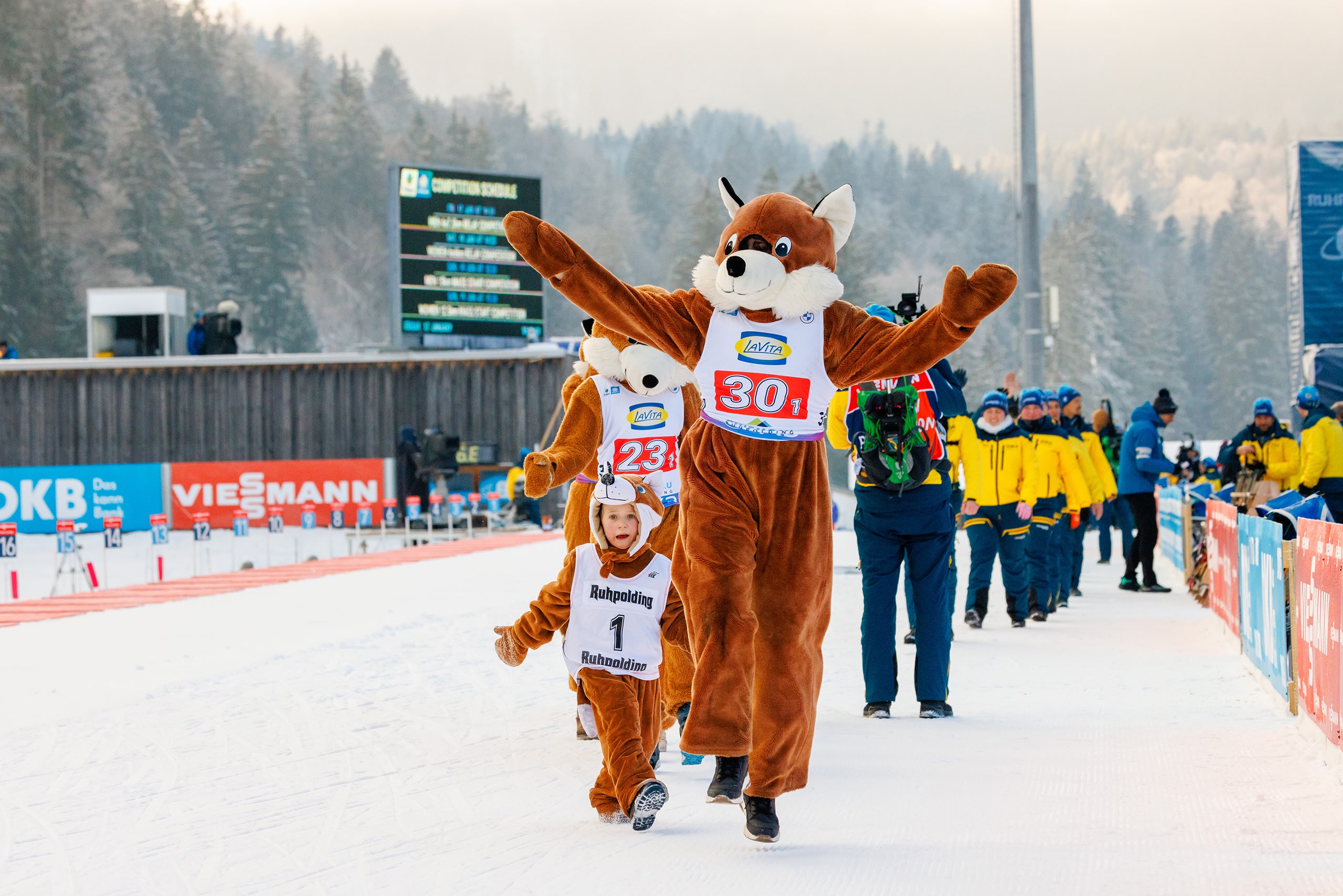Maskottchen Beppo läuft mit Helfern auf der Biathlon-Strecke und begrüßt die Zuschauer in der Chiemgau Arena.