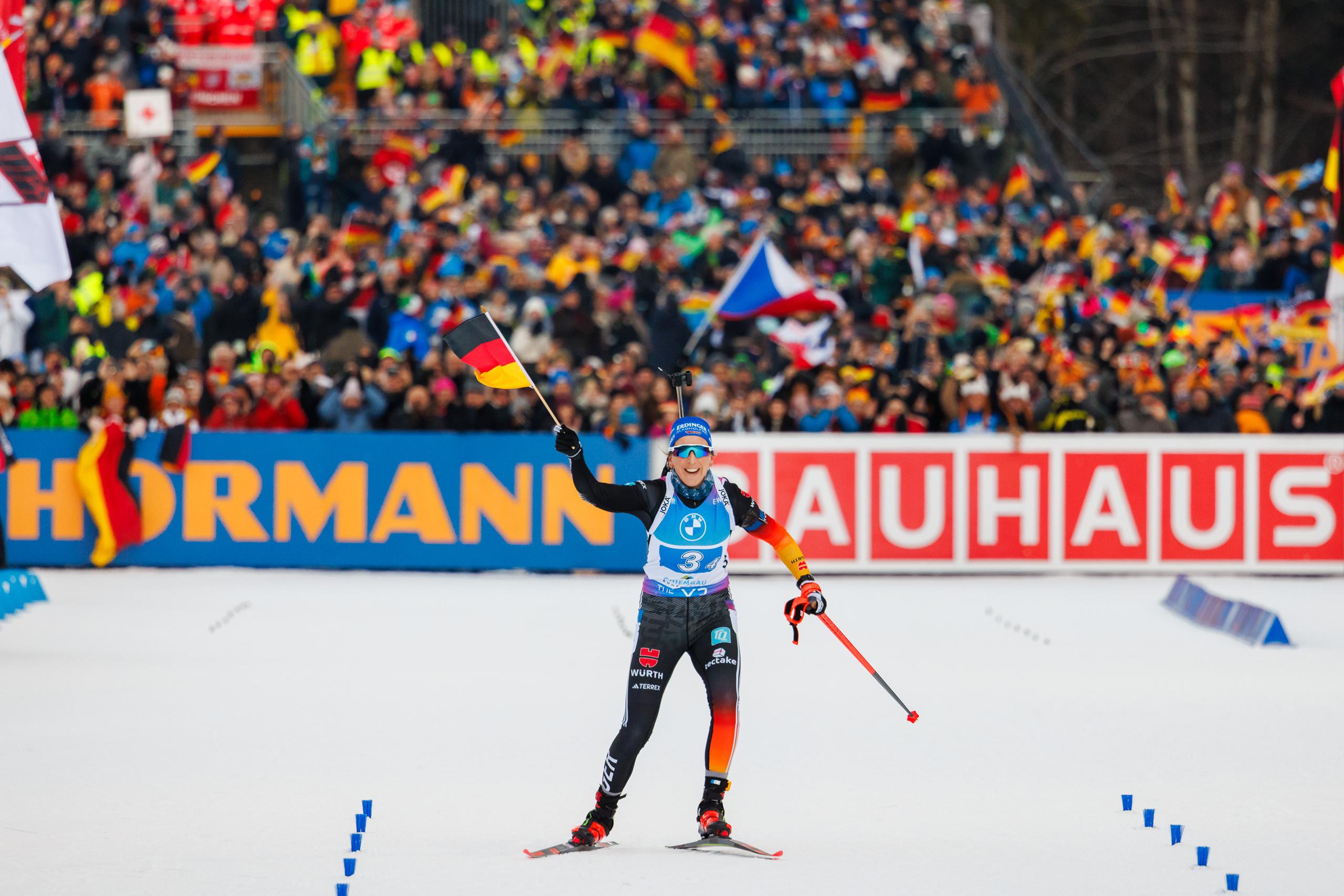 Newsletter_GT2A9653 Biathletin jubelt im Ziel mit einer Deutschlandfahne vor dicht gefüllter Tribüne in der Chiemgau Arena.
