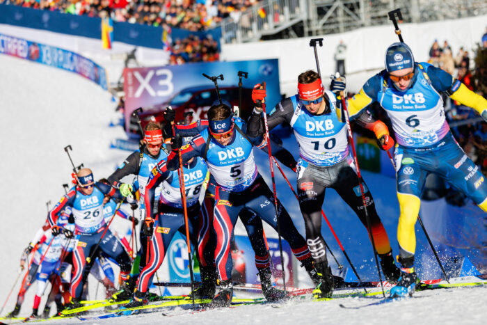 Staffel_Maenner_GT2A0245 Dicht gedrängte Biathleten kämpfen im Anstieg um Positionen, begleitet von jubelnden Zuschauern.