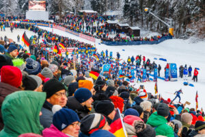 Großes Starterfeld der Männerstaffel läuft aus dem Stadionbereich los, umgeben von zahlreichen Zuschauern.