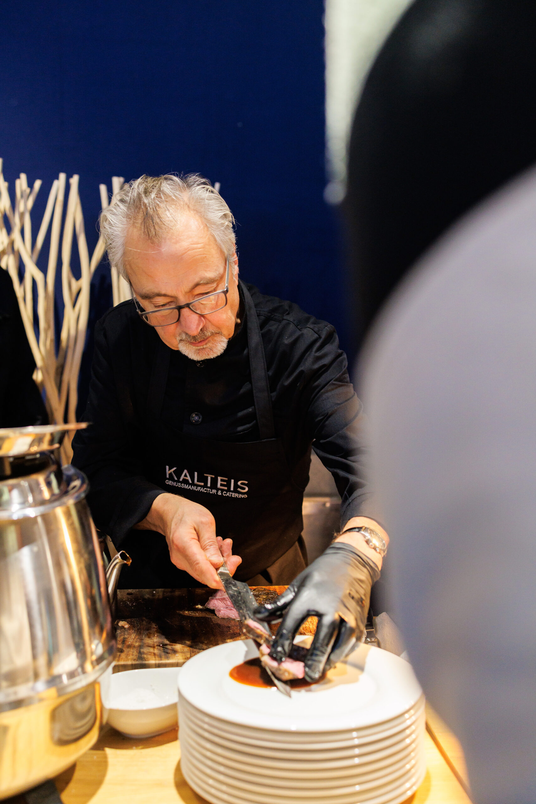 VIP_GT2A8447 Koch im VIP-Catering schneidet Fleisch und richtet Teller an einer Buffetstation an.