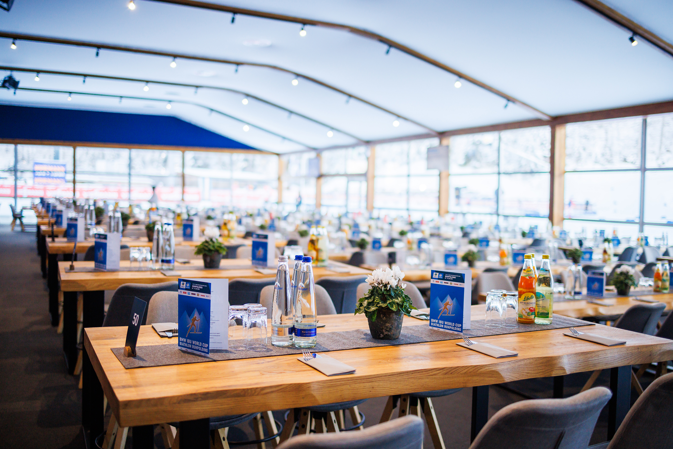 VIP_GT2A8839 Großer VIP-Bereich mit langen gedeckten Holztischen, Getränken und Dekoration im Zelt an der Chiemgau Arena.