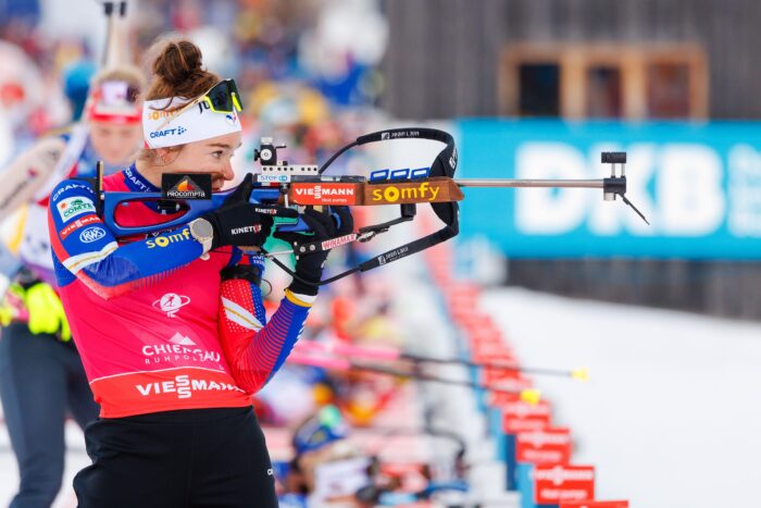 Verfolgung_Frauen_GT2A4658 Biathletin im Stehendschießen konzentriert am Schießstand, umgeben von weiteren Wettkampfteilnehmerinnen.
