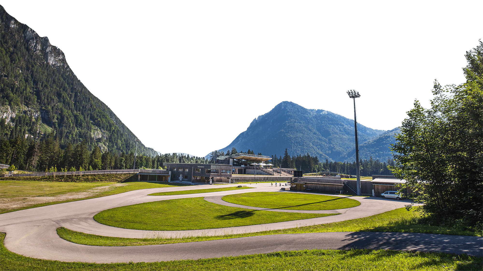 Sommeransicht der Chiemgau Arena Ruhpolding mit Rollerstrecke, Stadiongebäude und Alpenkulisse im Hintergrund.